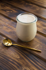 Homemade ryazhenka in the glass jar on the brown wooden  background. Fermented milk product. Location vertical.
