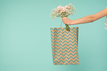 Girls hand holding shopping bag and tender flowers isolated over blue backgound