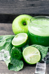 Green apple smoothie in glass and kale leaves on wooden table