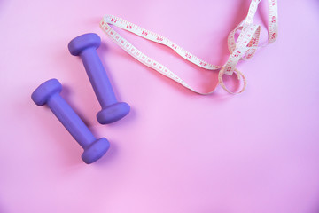 two purple dumbbells for fitness and measuring tape on a pink background, quarantine, workout at home