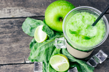 Green apple smoothie in glass and kale leaves on wooden table