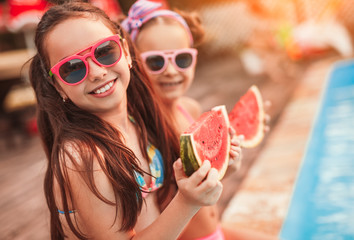 Happy sisters eating watermelon on poolside