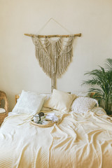 Modern romantic scandi boho style bedroom interior with decorative pillows, green plant and diy...