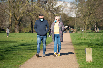 London, UK. Wednesday, 25 March, 2020. A couple wearing masks walking in a park in London. Photo:...