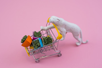 funny white tiger toy with shopping cart full of flowerpot on a soft pink background