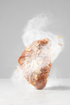 Fresh french croissant with almond and flying sugar powder on a light background.