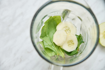 A top view of a blender with cucumber and spinach