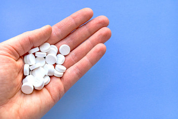 A handful of white pills in hand on a blue background close-up.
