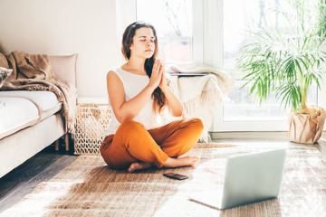 Woman doing yoga and watching tutorial lesson on laptop at home.