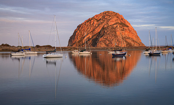 Morro rock reflects in the waters of Morro bay as boats are mored in still waters