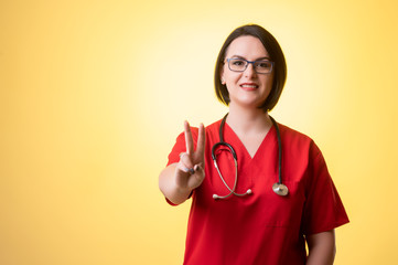 Beautiful woman doctor with stethoscope, wearing red scrubs showing victory