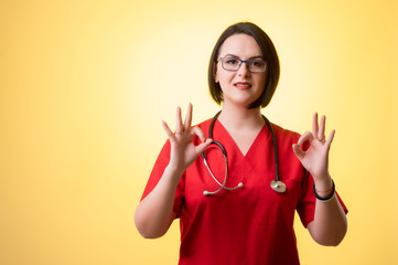 Beautiful woman doctor with stethoscope, wearing red scrubs showing double OK sign