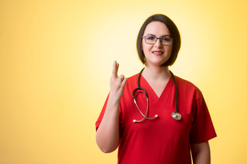 Beautiful woman doctor with stethoscope, wearing red scrubs showing good luck