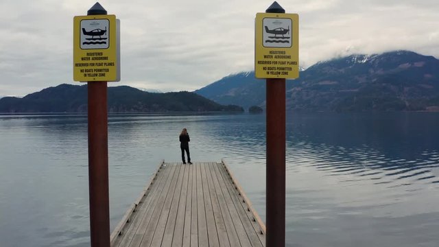 Woman standing on an old wooden water aerodrome pier, enjoying the view of Harrison Lake while waiting for the arrival of a hydroplane in Harrison Hot Springs, British Columbia, Canada