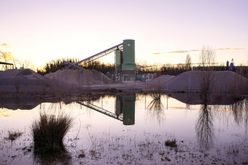 Conveyor over Gravel pit by sunset. Industrial landscape, building reflect in the water. Wetland of Rhine river, Germany. 