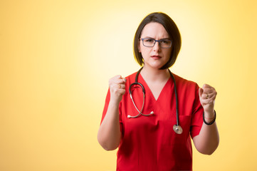 Beautiful woman doctor with stethoscope, wearing red scrubs showing fists