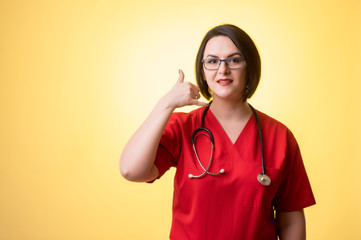 Beautiful woman doctor with stethoscope, wearing red scrubs showing call me gesture