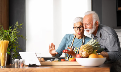 Senior couple in home kitchen looking at tablet