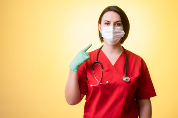 Beautiful woman doctor with stethoscope, wearing red scrubs wears a protective mask, with her finger pointed