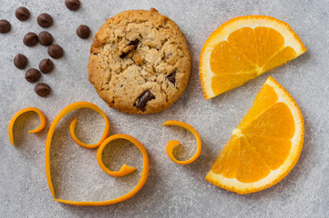 Chocolate chip and orange cookie. Orange peel in heart shape on grey stone background.