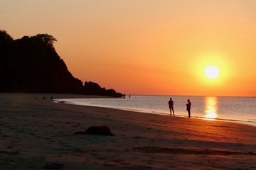 Sunset with orange sky at Nacpan beach with two girls and sleeping dog, El Nido, Palawan, Philippines