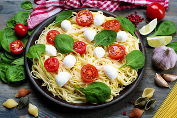 Pasta with cherry tomatoes, spinach and mozzarella on a brown clay plate. Traditional Italian recipes