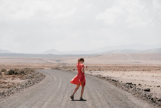 Happy girl wearing red dress dancing on road.