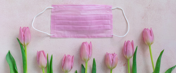 Pink protective surgical face mask and and fresh tulips background, selective focus, banner