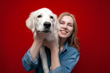 young beautiful girl holding a golden retriever puppy in her arms on a red background, close-up of the dogs face smiling, funny pets