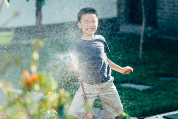 Cute boy playing with water hose in backyard