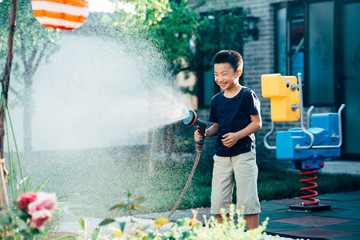 Cute boy playing with water hose in backyard