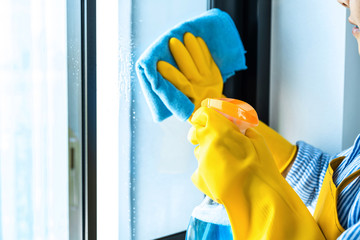 Wife housekeeping and cleaning concept, Happy young woman wiping dust using a spray and a duster while cleaning in glass at home