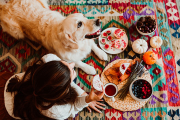 Young woman having a healthy breakfast lying on the floor at home while she is in quarentine during the covid19 crisis accompanied by her golden retriever. Lifestyle. Stay home