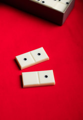 Two domino bones lie next to a gray box on a red fabric background. Plenty of room for text.