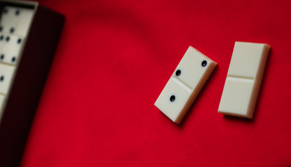 Two domino bones lie next to a gray box on a red fabric background. Plenty of room for text.