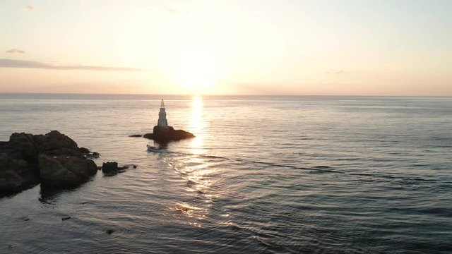 A drone flight at sunrise around a lighthouse and a small boat entering the sea, Ahtopol, Black Sea coast, Bulgaria