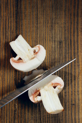 Cropped shot of blade of knife cutting champignons on wooden table. Vegetables, kitchen concept.