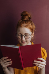 A redheaded girl with glasses and a book in her hands