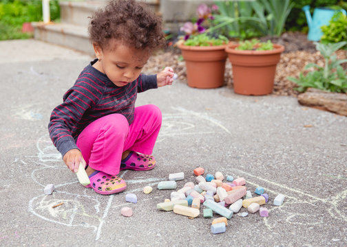 Cute toddler child drawing on the asphalt driveway with a large piece of chalk