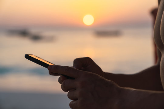 Hands holding a cellphone with the sunset background