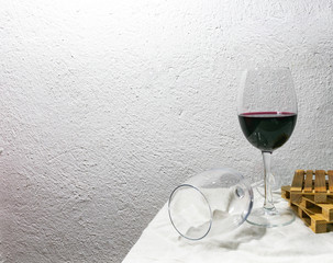Glass of red wine set on the white sheet with mini palletes standing near white  rough wall. Background image with blank space.