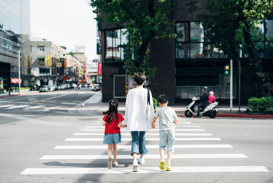 Mother holding daughter and son''s hands crossing road