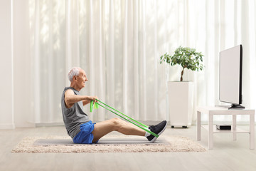 Senior man exercising with an elastic band in front of a tv at home