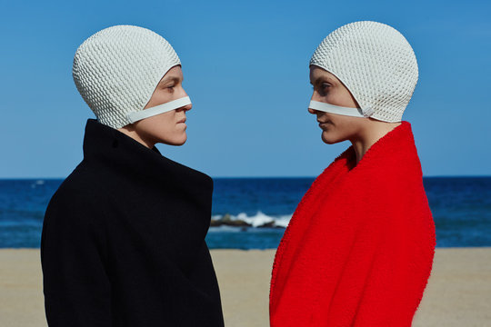 Conceptual portrait of women wearing bathing cap standing on beach