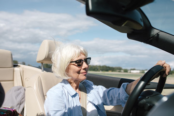 Relaxed older woman driving convertable car.