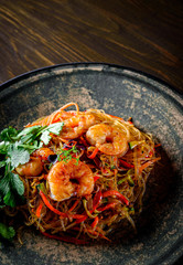 Stir fry noodles with vegetables and shrimps in plate on wooden table background