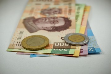 Many mexican pesos bills with coins on top spread over a surface