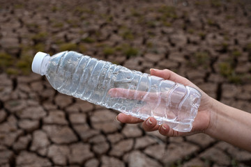 Close up woman hand holding the clear plastic bottle at crack soil background