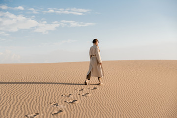 Close up of traces on sandy dune from woman in beige coat.