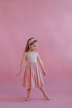 Lovely little girl in pink dress dancing by pink background